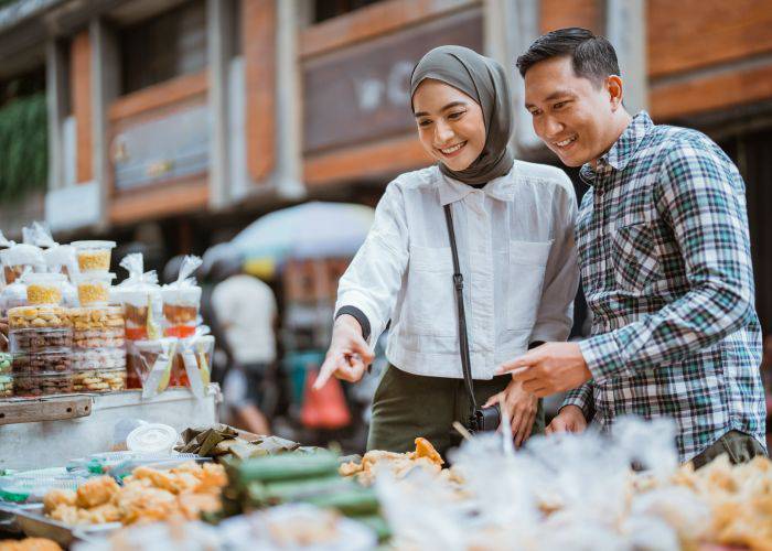 A woman of Muslim faith wearing a hijab and pointing at something on a food stall.